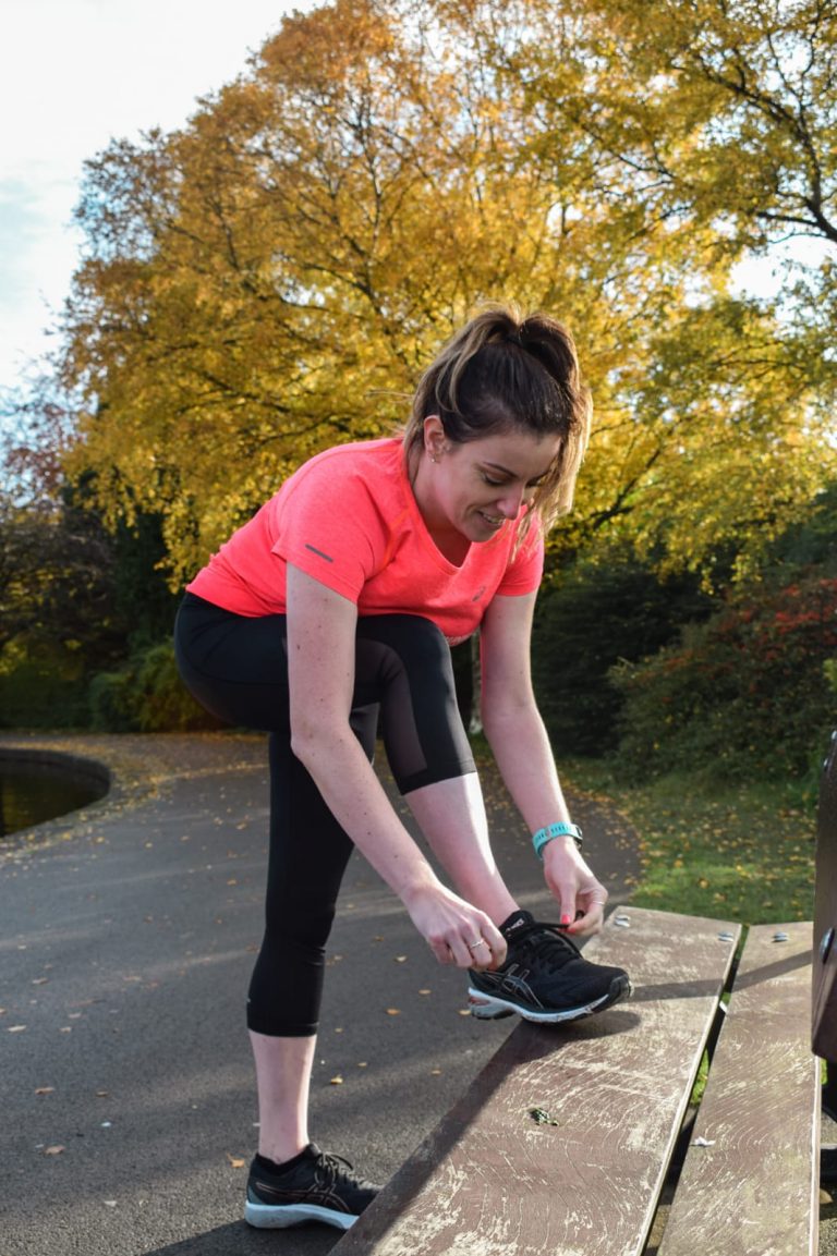 woman tying shoe lace on bench