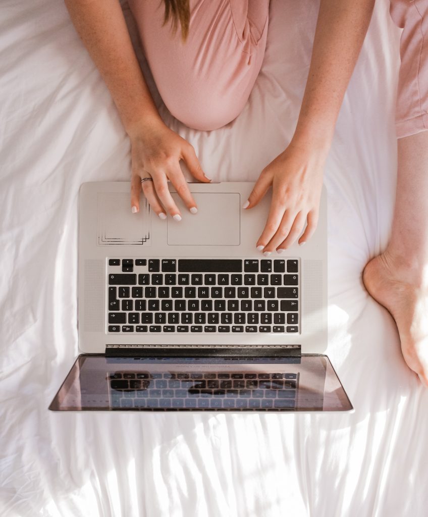 woman typing on laptop in bed
