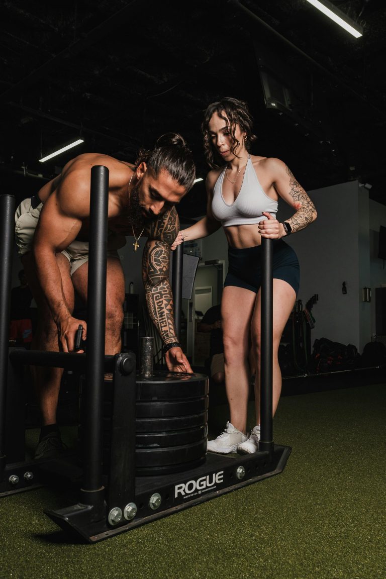 man and woman in gym sled push