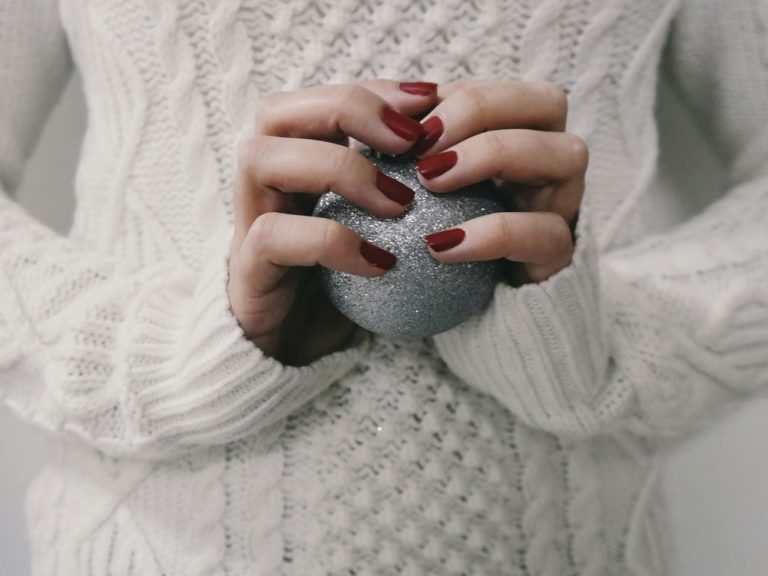 woman with red nails holding xmas bauble